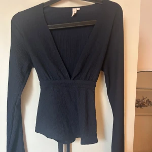 Mörkblå ribbad omlottopp - Snygg mörkblå ribbad omlottopp med långa ärmar och knytband i ryggen. Perfekt för en stilren look.