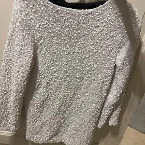 Vit paljettklänning med svart rosett - Säljer en glittrig vit klänning med paljetter och en elegant svart rosett i ryggen. Klänningen har trekvartsärmar och en öppen rygg som ger en stilren look. Perfekt för festliga tillfällen!