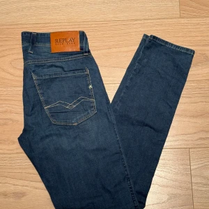 Replay jeans - Snygga mörkblå jeans från Replay med klassisk femficksdesign och en läderpatch med logga på baksidan. Jeansen har en slim passform och är perfekta för en stilren look. De är tillverkade i ett bekvämt denimtyg som ger en skön känsla hela dagen. Modellen heter anbass och storleken är 29/32