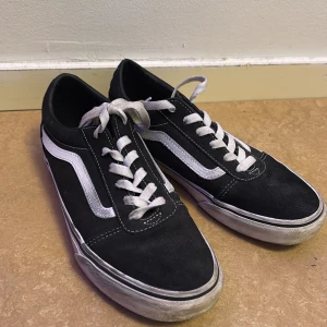 Svarta sneakers från Vans - Säljer ett par klassiska svarta Vans sneakers med vit sula och vit sidostrimma. Skorna har snörning och den ikoniska 'Off the Wall' loggan på hälen. Perfekta för en avslappnad stil.