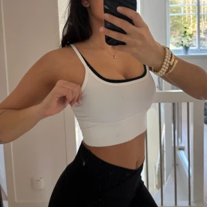 Vit croppad tränings topp - Vit croppad linnetopp med smala axelband och svart kantdetalj. Bra support och perfekt till gymmet! Bra med stretch så skulle säga att den passar både xs-m 💕