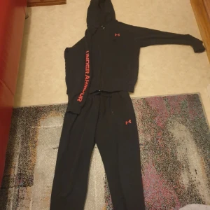 Svart hoodie och byxor från Under Armour - Säljer en svart hoodie och matchande byxor från under armour  tröjan har jag använt 4 gånger typ o har använt byxorna 7 gånger it ett ända fel de ser helt nya ut behöver  ba tveta de  pris kan diskuteras tröjan för 270kr byxorna 300 kr  men om någon  vill köpa båda då jag kan sälja de för 500kr