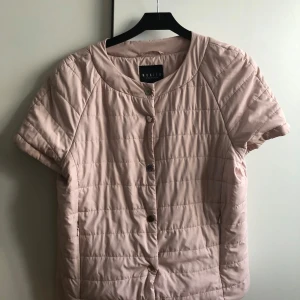 Beige quiltad jacka från Mohito - Säljer en beige quiltad jacka från Mohito med korta ärmar och knappar framtill. Perfekt för en stilren look. Jackan har en rund halsringning och är lätt vadderad för extra komfort. Passar för storlek s