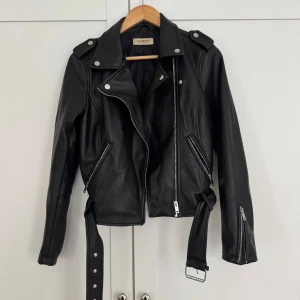 Svart skinnjacka - Snygg svart bikerjacka från Glamorous med dragkedjor och bälte. Jackan har en klassisk bikerstil och är i bra skick!