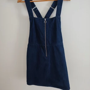 Mörkblå jeansklänning med dragkedja - Snygg mörkblå jeansklänning med justerbara axelband och dragkedja framtill. Storlek uppskattas till 40.