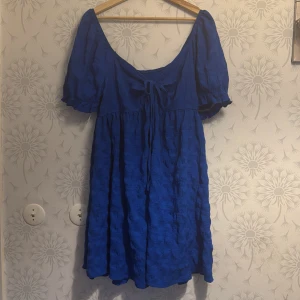 Blå klänning med knytband - Charmig blå klänning med korta ärmar och knytband framtill. Perfekt för en somrig look med sin luftiga design och vackra färg.