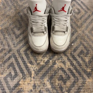Nike Air Jordans i vitt och grått - Säljer ett par klassiska Jordan 4s i White Oreo med Crease Skydd. Skorna har snörning och en ikonisk design som passar perfekt för sneakerheads. Skorna är ungefär 6 månader gamla utan några tydliga skador.