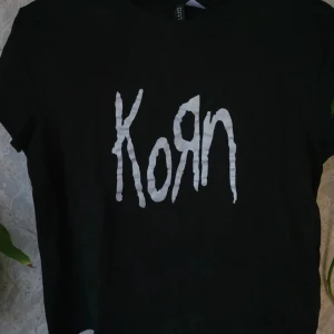 Svart t-shirt med Korn-tryck - Säljer en svart t-shirt från Gildan med det ikoniska Korn-trycket i vitt på framsidan. Perfekt för fans av bandet! T-shirten har en klassisk passform och korta ärmar.
