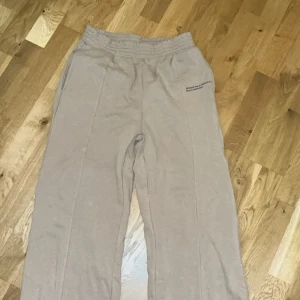 Beige mjukisbyxor med tryck - Säljer ett par bekväma beige mjukisbyxor med elastisk midja och ett tryck på sidan. Perfekta för en avslappnad stil. Storlek S