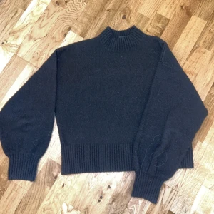 Svart stickad tröja från Monki - Säljer en svart stickad tröja från Monki. Tröjan har en hög krage och långa ärmar med ribbade muddar. Storlek S