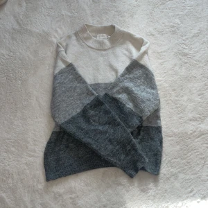 Grå och vit stickad tröja - Säljer en mysig stickad tröja i blockfärger av grått och vitt. Tröjan har en hög krage och långa ärmar, perfekt för kyliga dagar. Den är i storlek XS och passar utmärkt för både höst och vinter.