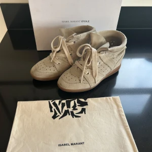 Beige sneakers från Isabel Marant - Snygga beige sneakers från Isabel Marant med snörning och perforerade detaljer. Skorna har en diskret kilklack och är tillverkade i mocka, vilket ger en lyxig känsla. Perfekta för en stilren och avslappnad look.