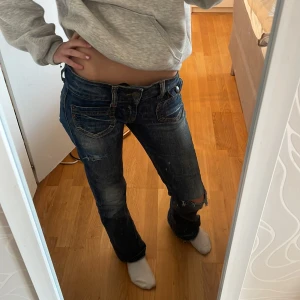 Blå jeans med slitningar - Säljer ett par blå jeans med slitningar och låg midja. De har en klassisk femficksdesign och en straight passform. Perfekta för en avslappnad stil.