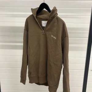 Beige halv zip från Les Deux - Säljer en stilren beige halv zip från Les Deux med dragkedja vid halsen. Tröjan har långa ärmar och en broderad logotyp på bröstet. Perfekt för en avslappnad look.