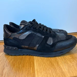 Valentino rockrunners  - Snygga svarta sneakers från Valentino med ett diskret camouflage-mönster. Skorna har snörning och är dekorerade med nitar på sulan. Tillverkade i en kombination av skinn och mocka för en lyxig känsla. Uk 7 hör av er vid frågor och tankar 
