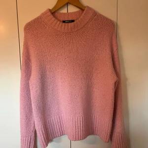Rosa stickad tröja från Gina Tricot - Mysig rosa stickad tröja från Gina Tricot med ribbade detaljer vid ärmslut och nederkant. Perfekt för kyliga dagar. Tröjan har en avslappnad passform och långa ärmar.