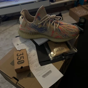 Adidas Yeezy sneakers - Säljer ett par Adidas Yeezy sneakers i en unik färgkombination av beige, blå och rosa. Skorna har en stickad ovandel med snörning och en bekväm sula. Perfekta för dig som vill ha en stilren och modern look.
