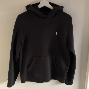 Svart hoodie från Ralph Lauren - Säljer en stilren svart hoodie från Ralph Lauren med den klassiska loggan på bröstet. Tröjan har en bekväm passform med långa ärmar och en praktisk magficka. Perfekt för en avslappnad look.                                                     Svarar snabbt på frågor!