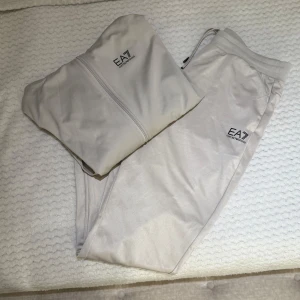 Vit träningsjacka från Emporio Armani - Säljer ett beiget set från Emporio Armani med, koftan har en snygg logga på bröstet, har luva och en Armani logga på ryggen ( bild 2 ) Säljs pågrund av att det ej används längre. Detta säljs i Set och byxorna är o storlek L, passar M, koftan är i storlek L och passar också M. Pris : 400kr och priset kan diskuteras🙂 Setet har inga skador, och fler bilder kan skickas om det önskas!
