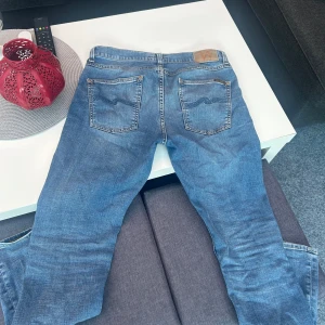 Blåa jeans från Nudie Jeans - Säljer ett par snygga blå jeans från Nudie Jeans. Väldigt bra skick, köpta på Kennedies för 1600kr. Skriv för mer info!