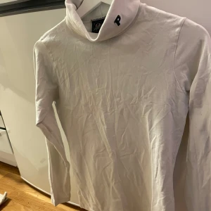 Vit polotröja från Peak Performance - Säljer en stilren vit polotröja från Peak Performance. Tröjan har en hög krage med ett broderat 'P' på sidan. Pris kan diskuteras vid snabb affär (S men passar även  M)