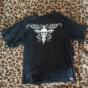 Svart t-shirt med dödskallemotiv - Cool svart t-shirt med ett stort vitt dödskallemotiv och dekorativa detaljer på framsidan. Baksidan har texten 'fighter' i ett stiliserat typsnitt. Perfekt för en edgy look.