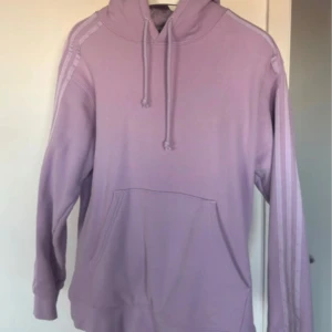 Lila hoodie från Ivy Park x Adidas - Säljer en snygg lila hoodie från Ivy Park med klassiska ränder längs ärmarna. Tröjan har en stor ficka framtill och justerbar huva med dragsko. Perfekt för en avslappnad stil.