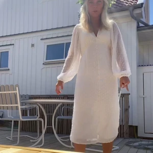 Vit långklänning med volangdetaljer - Säljer en superfin vit långklänning med v-ringning och långa ärmar. Klänningen har en elegant slits framtill och fina volangdetaljer på ärmarna. Perfekt för sommarens fester eller midsommarfirande! 