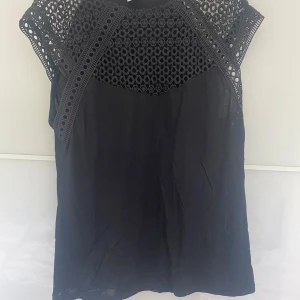 Svart topp med spetsdetaljer från H&M - Säljer en elegant svart topp från H&M med vackra spetsdetaljer vid halsen och ärmarna. Toppen är ärmlös och har en luftig passform, perfekt för både vardag och fest. Materialet känns mjukt och bekvämt mot huden.