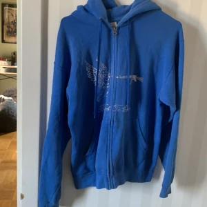 Blå hoodie med dragkedja och strassdetaljer - Säljer en snygg blå hoodie med dragkedja och coola strassdetaljer på framsidan. Den har en ängel och texten ' best yet to come ' i glittrande stenar. Perfekt för en avslappnad stil med lite edge. Den är i storlek S och passar perfekt för höst och vår. pris kan diskuteras 