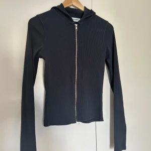 Svart ribbad hoodie med dragkedja - Säljer en snygg svart ribbad kofta med dragkedja framtill. Den har långa ärmar och en skön huva, perfekt för både höst och vår. Passar till alla tillfällen när du vill vara både bekväm och stilren. Lagom stretchig, passar Xs-M.