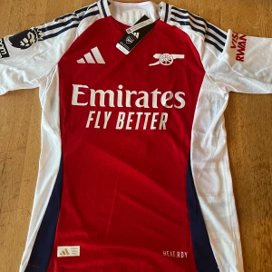 Sakna Arsenal 24/25 hemmatröja  - Säljer denna fräscha helt nya arsenal  hemma törjan med tagg för uppkommande säsong 24/25 med saka På ryggen och premiur Leauge loggan på Armen. 