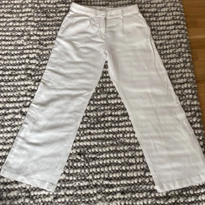 Vita linnebyxor från H&M - Säljer ett par snygga vita linnebyxor från H&M i storlek 38. De är tillverkade i ett skönt linneblandat material som passar perfekt för sommaren. Byxorna har en avslappnad wide fit och är högmidjade. Perfekta för både vardag och fest!