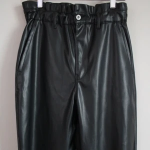 Svarta skinnbyxor med hög midja - Säljer ett par snygga svarta skinnbyxor med hög midja. Byxorna har en loose passform och är perfekta för en cool och stilren look. De har fickor både fram och bak samt en knapp och dragkedja i midjan. Perfekta för höst och vinter!