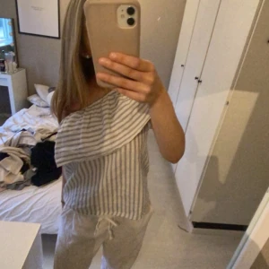 Randig offshoulder topp - Säljer en superfin randig offshoulder topp i ljusblått och vitt. Den har en snygg volangdetalj över axeln och är perfekt för sommardagar. Toppen är i ett lätt och bekvämt material, perfekt för en avslappnad men stilren look.