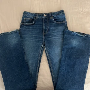 Blå jeans från Zara - Säljer ett par snygga booutcut blå jeans från Zara i storlek EUR 34. De är i bra skick och har en klassisk femficksdesign med dragkedja och knapp framtill. Perfekta för både vardag och fest! 💙