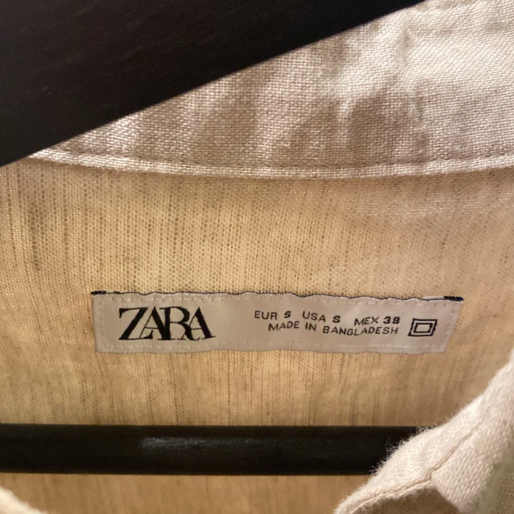 Säljer en stilren beige skjorta från Zara i storlek S. Skjortan är långärmad och har en klassisk krage med knappar framtill. Den är tillverkad i ett lätt och bekvämt material, perfekt för både vardag och fest. Skjortan har en bröstficka som ger en extra touch av stil.. Skjortor.