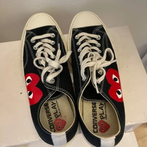 Svarta Converse Play sneakers med röda hjärtan - Säljer ett par svarta Converse Play sneakers med de ikoniska röda hjärtan på sidorna. Skorna har vita snören och vita sulor. De är i bra skick med lite slitage på sulorna. Perfekta för en casual look eller för att lägga till en rolig detalj till din outfit!