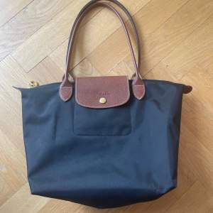 Säljer denna svarta longchamp väska med bruna och guldiga detaljer som är perfekt som skolväska men passar även till annat! Den är helt oanvänd Nypris - 1400kr