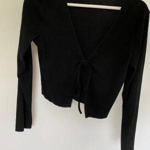 Svart långärmad topp från Shein - Säljer en svart långärmad topp från Shein. Den har en v-ringad design med knytning framtill, vilket ger en snygg och stilren look. Perfekt för både vardag och fest!