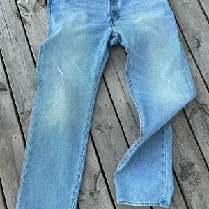 Levi's 501 jeans i ljusblå denim - Säljer ett par klassiska Levi's 501 jeans i ljusblå denim. De har en straight passform och är tillverkade i slitstarkt bomullsmaterial. Jeansen har den ikoniska knäppningen med knappar och en snygg vintage-look med lätt slitna detaljer. Perfekta för en avslappnad stil!