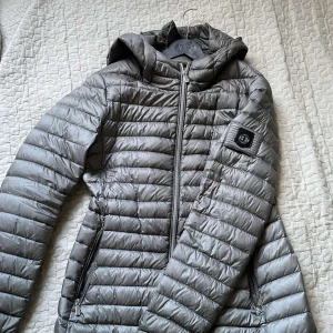 Grå Hollies Dunjacka - Säljer min metallic grå dunjacka från Hollies. Storleken är 40 men passar de med strl M, det går även att spänna åt i midjan. Den har ett litet hål i fickan men inte något.  som man lägger märke till eller gör någon skillnad! Pris går att diskutera