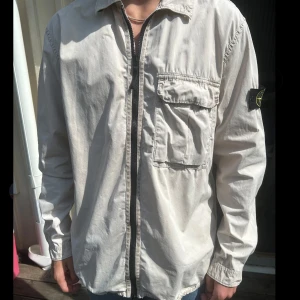 Stone Island Overshirt  - Stone Island Overshirt Storlek L. Inköpt för några år sedan men säljer pga den hängt i garderoben senaste 3 år. Har fläck/fläckar, se bild 4 för både fläck och hur det ser ut när overshirten bärs. Kan försvinna med kemtvätt ej, testat därav pris.
