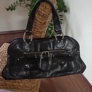Svart skinnväska från Luisa Cerano - Säljer en snygg svart skinnväska från Luisa Cerano. Väskan har en cool design med flera dragkedjor och detaljer i metall. Perfekt för både vardag och fest! Den är i bra skick med lite slitage på kanterna, men det ger bara mer karaktär. Passa på att köpa denna stiliga väska!
