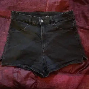 Säljer ett par snygga svarta högmidjade jeansshorts. De har en klassisk femficksdesign och en liten slits på sidorna som ger en extra touch. Perfekta för sommardagar eller en avslappnad utekväll. Passar till allt och är superbekväma!