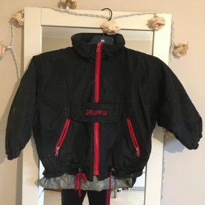 Svart jacka från Mini Kids - Säljer en cool svart jacka från Mini Kids med röda dragkedjor och detaljer. Jackan har en quiltad insida som gör den perfekt för kyligare dagar. Den två sidor fickor.storlek 104