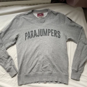 Parajumpers sweatshirt - En grå Parajumpers sweatshort med en stor logotyp på framsidan. Tröjan har en rund halsringning och långa ärmar. Tröjan är i väldigt bra skick, inga anmärkningar.