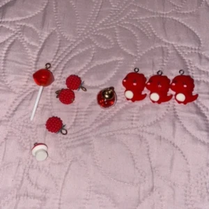 Söta röda örhängen och berlocker - Ett set med olika röda smycken, inklusive örhängen och berlocker. Det finns ett par örhängen som ser ut som röda klubbor, ett par med röda bär och några små röda figurer. Perfekt för att lägga till en lekfull touch till din outfit!