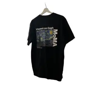 Säljer en svart t-shirt med ett coolt tryck av Vincent van Goghs 'Stjärnenatt' på baksidan. T-shirten är från MoMA och har en liten text på framsidan. Perfekt för konstälskare som vill ha något unikt i garderoben!