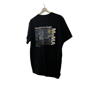 Svart t-shirt med Vincent van Gogh tryck - Säljer en svart t-shirt med ett coolt tryck av Vincent van Goghs 'Stjärnenatt' på baksidan. T-shirten är från MoMA och har en liten text på framsidan. Perfekt för konstälskare som vill ha något unikt i garderoben!